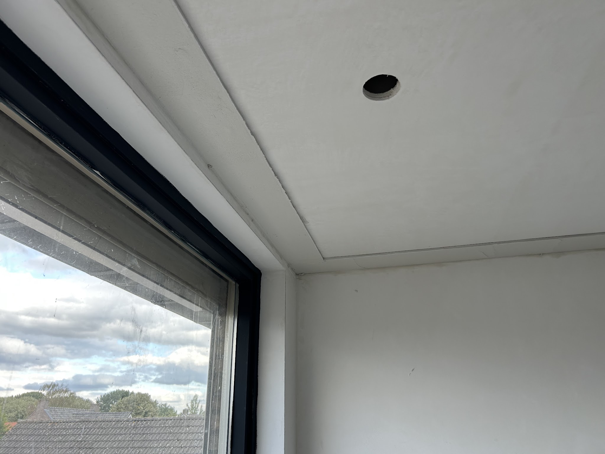 Glad gestuct plafond en dagkant bij een groot raam met donker kozijn